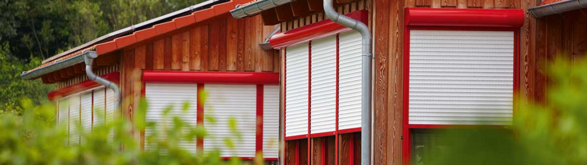 mehrere rot-weiße Rollläden an einem braunen Haus