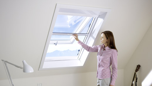 Frau zieht ein Insektenschutzgitter an einem Dachfenster nach unten